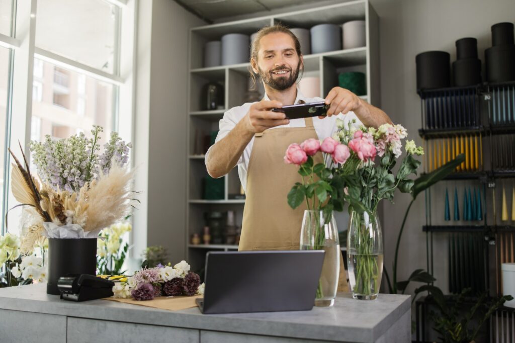 Attractive young male florist make bouquet and taking photo on smart phone for social media.