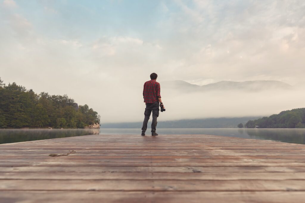 Landscape photographer at lake pier in misty morning