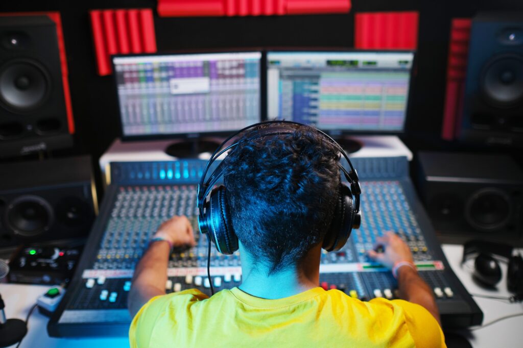 Rear view of sound engineer sitting in front of sound mixing console.